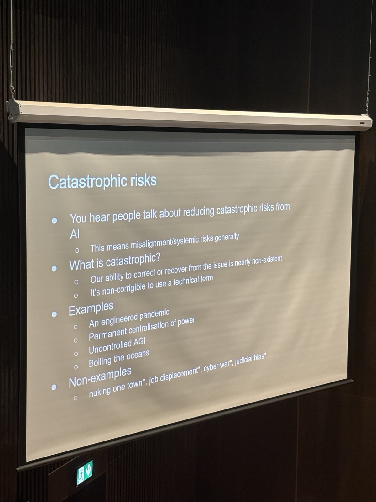 Slide titled Catastrophic risks, defining catastrophic as non-corrigible, with examples like an engineered pandemic and uncontrolled AGI, and non-examples like job displacement