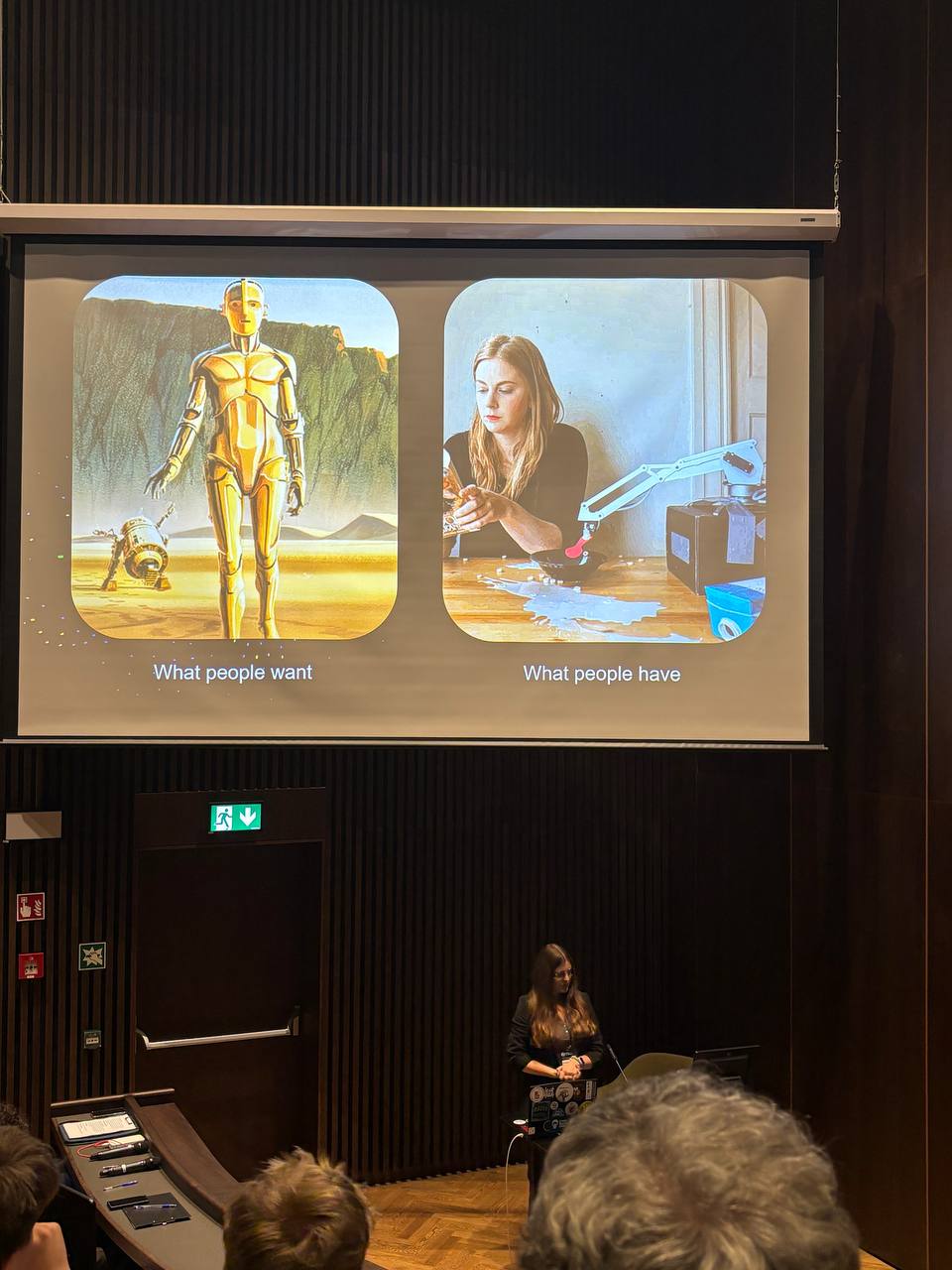 Karolina Korgul presenting a slide comparing What people want, a golden humanoid robot from Star Wars concept art, with What people have, Simone Giertz next to her breakfast robot spilling milk across the table